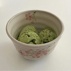 a bowl filled with green ice cream on top of a white table next to a pink flower