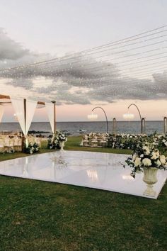 an outdoor wedding setup with white flowers and draping on the grass near the ocean