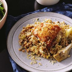 a white plate topped with chicken and rice next to a bowl of salad on a table