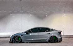 a grey car parked in a parking lot next to a white wall and some lights