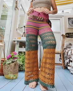 a woman wearing crocheted pants and sandals standing in front of a window with her hands on her hips