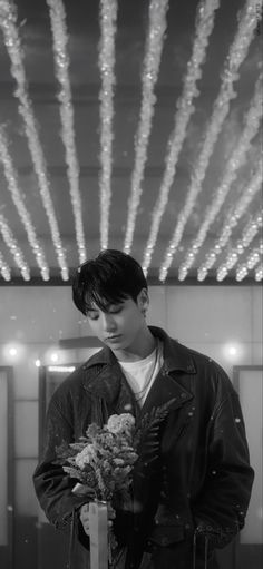 black and white photograph of a young man holding flowers in front of a ceiling with lights