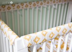 a baby crib with a yellow and white blanket on it's bed rail