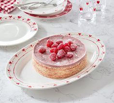 there is a cake with raspberries on the top and two plates next to it