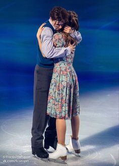 two people hugging each other on an ice skating rink in front of a blue background