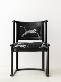 a black chair with zebra print on the back and armrests, sitting against a white wall