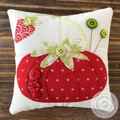 a red pumpkin pillow with buttons on the front and back, sitting on a wooden surface