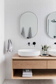 two round mirrors are above the sinks in this modern bathroom with white tiles on the walls