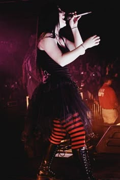 a woman in black and red striped dress holding a microphone while standing next to a stage