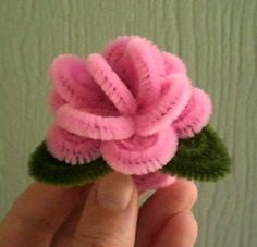 a hand holding a pink flower with green leaves