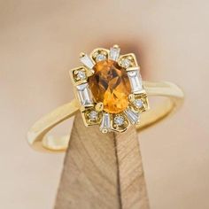 an orange and white diamond ring sitting on top of a wooden stand