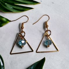 Recently worn by actress Rosa Arredondo in her role as Francey on the hit show, "So Help Me Todd", these stunning Gold Triangle Earrings, feature a mesmerizing Aquamarine glass faceted drop.  These earrings are truly an experience with golden, geometric, stainless triangles reflecting the light and capturing attention with every movement. The Aquamarine glass drop, in a beautiful, oceanic blue is the heart of these earrings, symbolizing tranquility, clarity, and elegance.  Treat yourself to the Gold Faceted Crystal Earrings For Party, Faceted Dangle Jewelry For Party, Faceted Brass Drop Earrings, Faceted Teardrop Crystal Earrings For Parties, Metal Earrings With Faceted Beads For Party, Metal Earrings With Faceted Beads, Glass Faceted Beads Earrings For Gift, Glass Earrings With Faceted Beads As A Gift, Glass Earrings With Faceted Beads For Gift