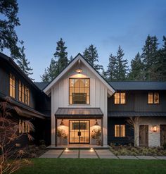 a large house with lots of windows and lights on it's front porch, in the evening