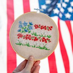 someone is holding up a cross stitched american flag with red, white and blue flowers