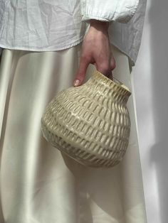 a close up of a person's hand holding a vase on a white cloth