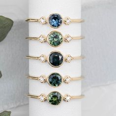 five different colored rings on top of a white napkin with green leaves in the background