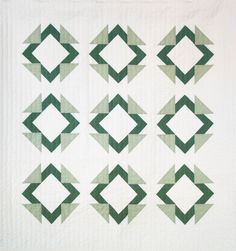 a quilted wall hanging with green and white geometric designs on the front, along with two rows of smaller squares