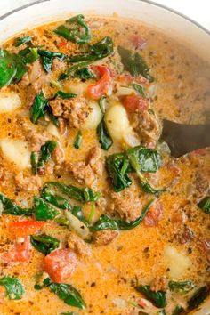 a pot filled with meat and vegetables on top of a white countertop next to a wooden spoon