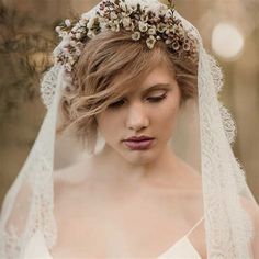 a woman wearing a veil with flowers in her hair is looking down at the camera