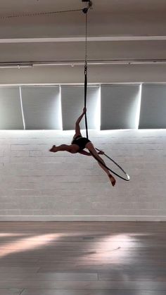 a woman hanging upside down on a rope in an empty room with white brick walls