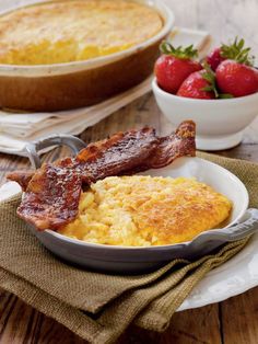 bacon and eggs in a pan on a table with strawberries next to the casserole