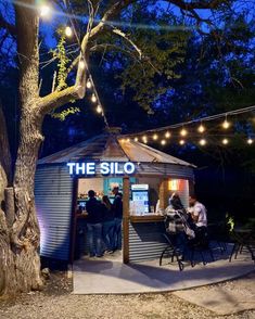 people sitting at tables in front of a small building with the word the silo on it