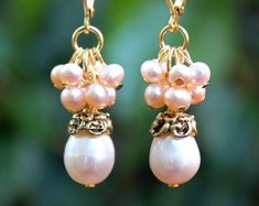 "This lovely pair of earrings features a luminous champagne freshwater pearl, which are accented with an ornate pewter bead cap, plated in 24 karat gold. This striking color combination is offset with beautiful clusters of champagne freshwater pearls. Hanging from a surgical steel lever-back, it measures 1 ¼\" in length. Pearls are known to symbolize purity of heart & mind. Pearls stimulate spiritual transformation, wisdom, integrity and pure love. They bring out the best qualities that rest wit Pink Pearl Charm Wedding Earrings, Pink Pearl Charm Earrings For Wedding, Elegant Pink Pearl Earrings For Celebration, Elegant Cream Jewelry With Dangling Beads, Pink Pearl Earrings For Wedding, Nickel-free Gold Pearl Earrings For Wedding, Nickel-free Pearl Earrings For Weddings, Pearl Cluster Earrings, Hematite Crystal