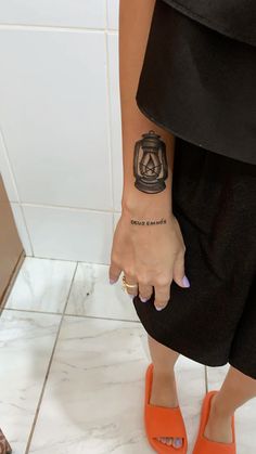 a woman with a small tattoo on her left arm and orange shoes is standing in front of a white tile wall