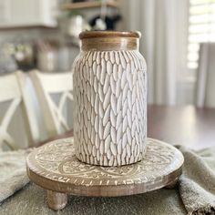 a white vase sitting on top of a wooden stand next to a table with chairs in the background