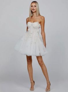 Embrace your inner romantic with this White Strapless Sweetheart Neck Corset Floral Appliqué Layered Tulle Mini Dress. This dreamy mini dress features a strapless sweetheart neckline, beautifully highlighting the décolletage for a feminine and elegant look. The corset bodice, with its tie-back detail, cinches the waist, offering a flattering silhouette and structured fit. Intricately designed floral appliqués adorn the bodice, adding a touch of whimsy and elegance. Layers of soft tulle create a Chic Mini Length Corset Dress For Wedding, Chic Strapless Tulle Corset Dress, Summer Wedding Mini-length Corset Dress, Sheer Bodice Organza Mini Dress For Wedding, Wedding Mini Dress With Sheer Bodice Organza, Summer Cocktail Corset Dress With Tulle Skirt, Spring Bridesmaid Mini Corset Dress, Chic Tulle Corset Dress, Spring Mini Dress With Sheer Bodice And Sweetheart Neckline