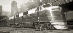 a silver train traveling down tracks next to tall buildings