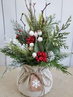 a vase filled with greenery and berries on top of a burlap bag