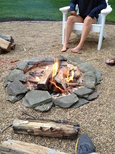 a man sitting in a chair next to a fire pit with logs on the ground