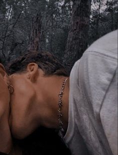 a man and woman kissing in the woods with their heads touching each other's foreheads