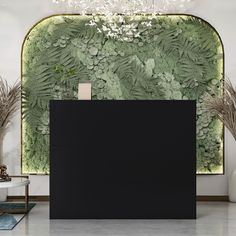 a black counter sitting in front of a wall with plants on it and a chandelier hanging from the ceiling