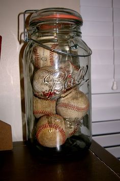 a glass jar filled with baseballs sitting on top of a wooden table next to a wall