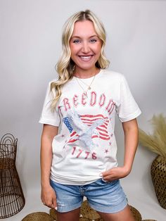 Freedom Eagle 1776 Oversized Ivory Relaxed Fit Graphic Tee Introducing our Freedom Eagle American Flag 1776 Graphic T-Shirt – the perfect piece to showcase your patriotic spirit with vintage flair! This vintage white t-shirt features a bold and iconic design with a majestic eagle, the American flag, and the year 1776, celebrating the birth of our nation. The striking red, white, and blue colors pop against the classic ivory backdrop, making it a standout piece for any patriotic occasion. Crafted White T-shirt With American Flag Print For Spring, White T-shirt With American Flag, White T-shirt With American Flag Print, White American Style Tops For Memorial Day, American Style T-shirt With Flag Print For Spring, White T-shirt With American Flag For Spring, Vintage American Flag Print Cotton T-shirt, Americana Style Flag Print T-shirt For Spring, White American Flag Relaxed Fit Top