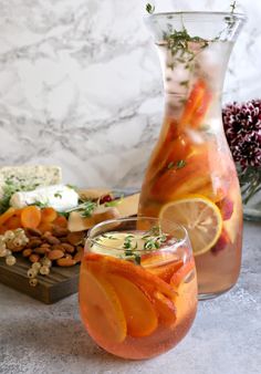 two glasses filled with drinks next to a vase full of fruit and nuts on a table