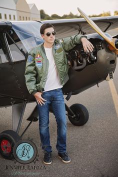 a man standing in front of an airplane with his hand on the wing and wearing sunglasses