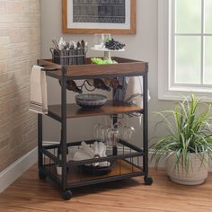 a kitchen cart with wine glasses on it in front of a brick wall and potted plant