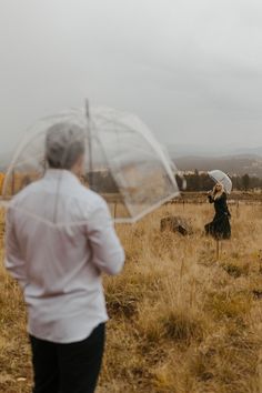 a woman holding an umbrella while walking through a dry grass field with another person in the background