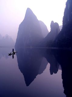 a person in a kayak paddling through the water with mountains behind them on a foggy day