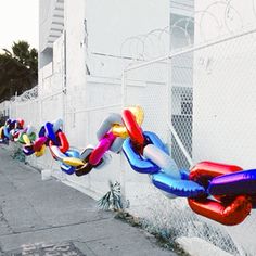 a row of colorful balloons tied to a chain on the side of a building next to a fence