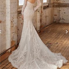 the back of a wedding dress with long sleeves and an open neckline, in front of a brick wall