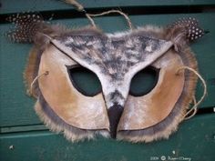 an owl mask with feathers on it's head hanging from a green wooden wall