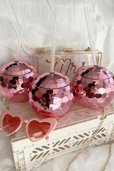 three shiny pink balls with heart shaped sunglasses on top of a white tray next to a purse