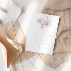 a white and gold wedding stationery with ribbon on the side, laying on a bed