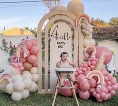 a baby is sitting in a high chair surrounded by balloons and archs that spell out the name amelie turns one