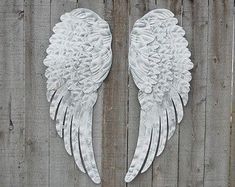 two white angel wings sitting on top of a wooden fence next to eachother