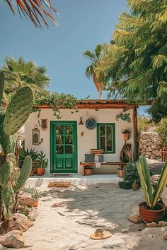 a small white house with green doors surrounded by cactus and cacti in front of it